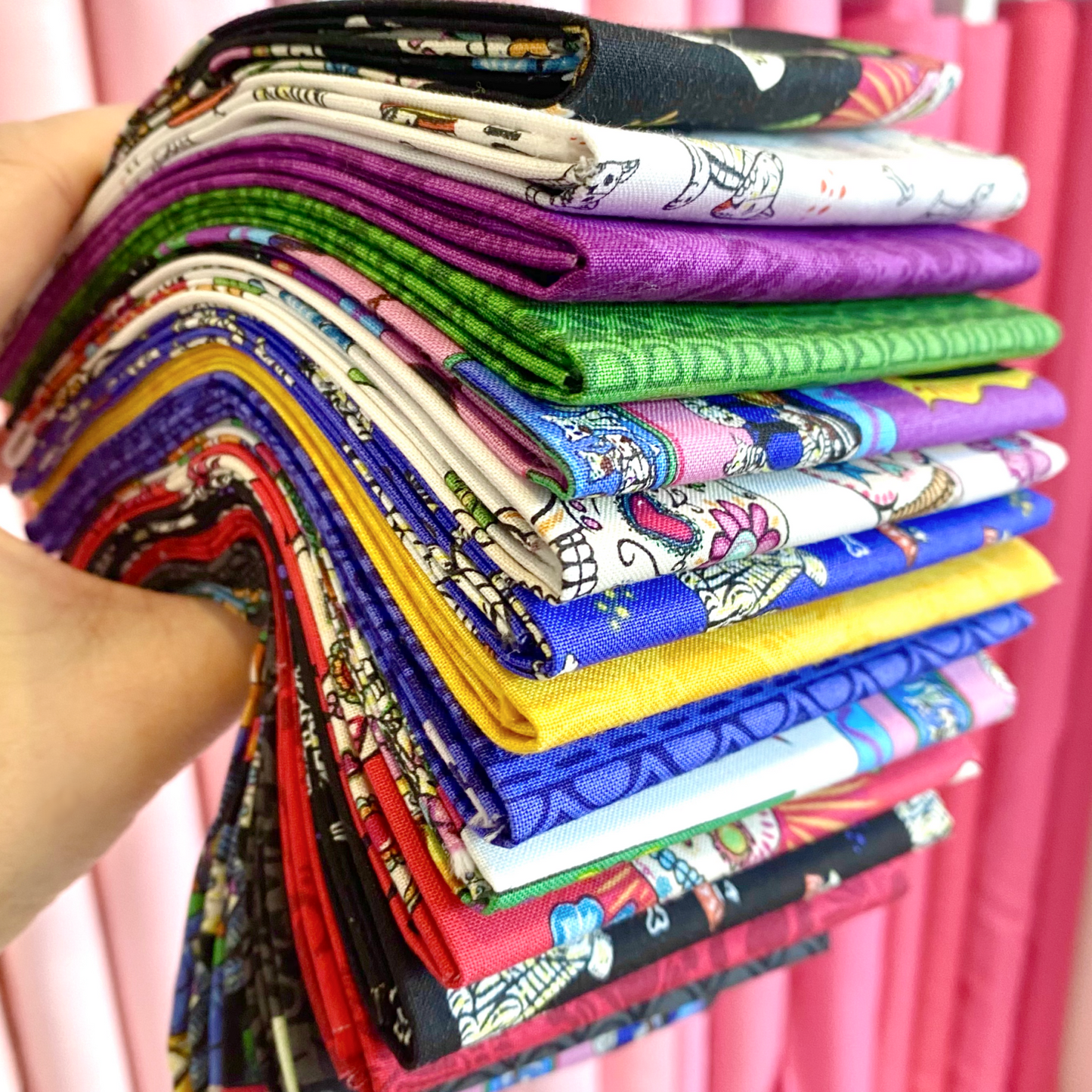 Hand holding folded fabric fat quarters with colorful skull-themed prints