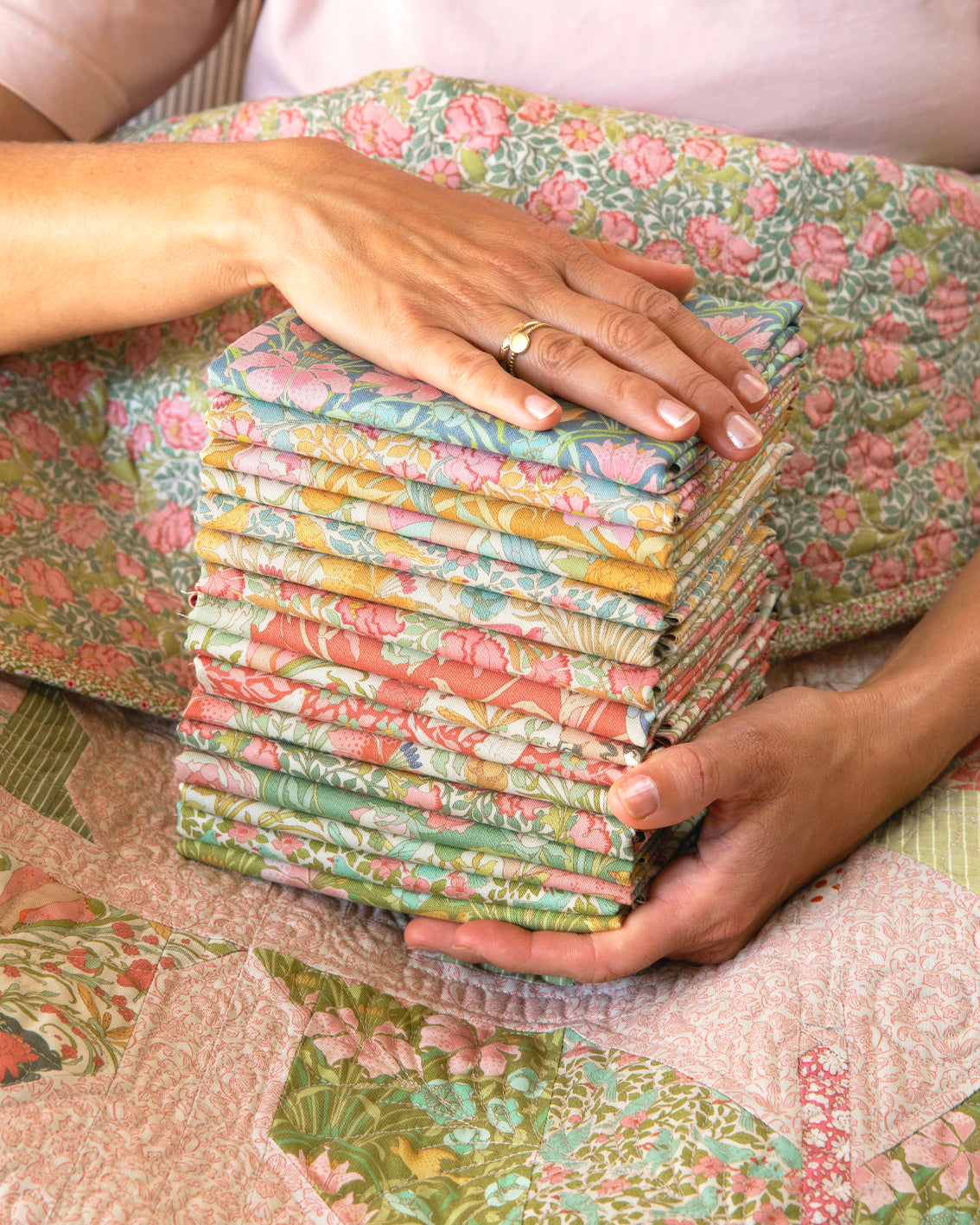 Quilt fabric stack held by hands, pastel bird and floral fat eighths