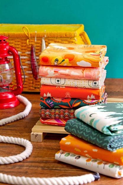 Fat quarter bundle of 12 folded fabrics with lake, tree, and animal motifs in orange and green