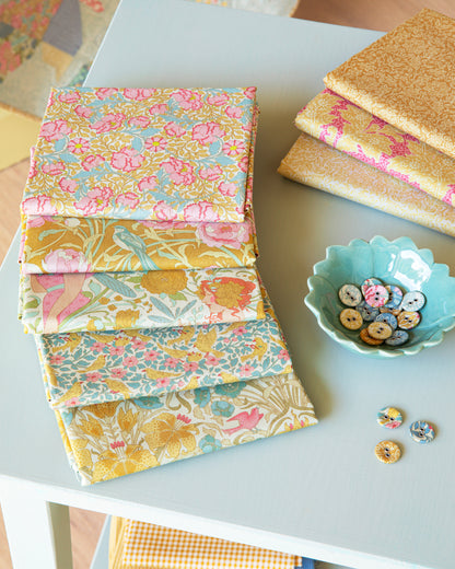 Coordinating fat quarter fabric stacks with floral and bird prints in pink, teal, mustard