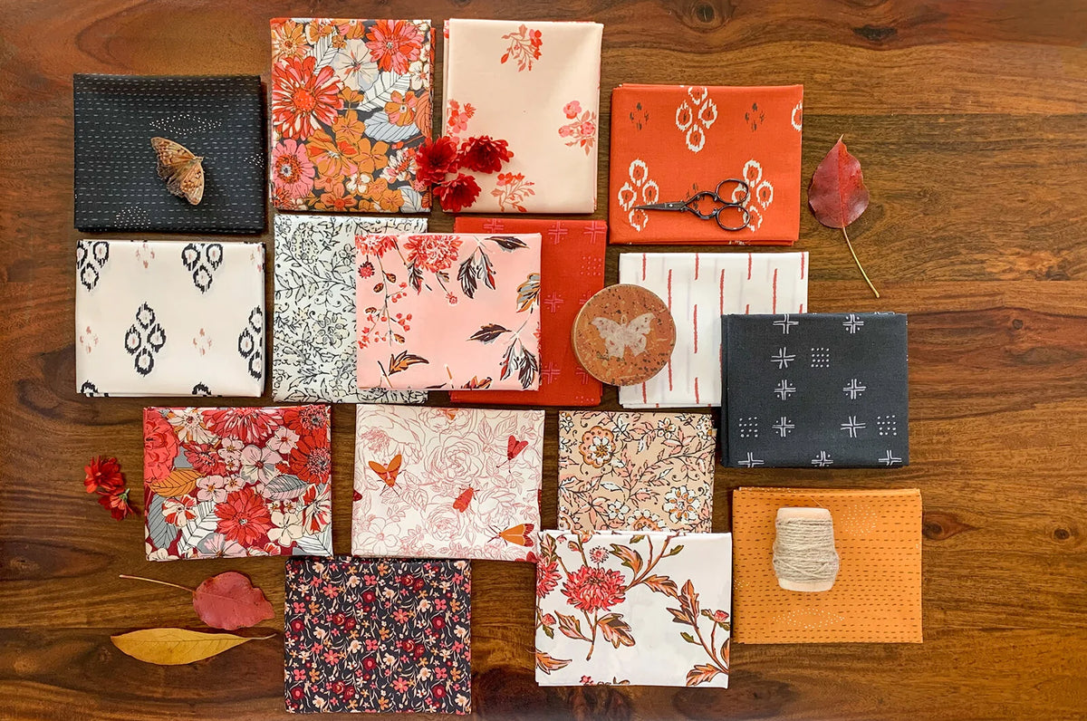 Assorted fat quarter fabrics laid flat: floral, leaf, and geometric prints on wood surface