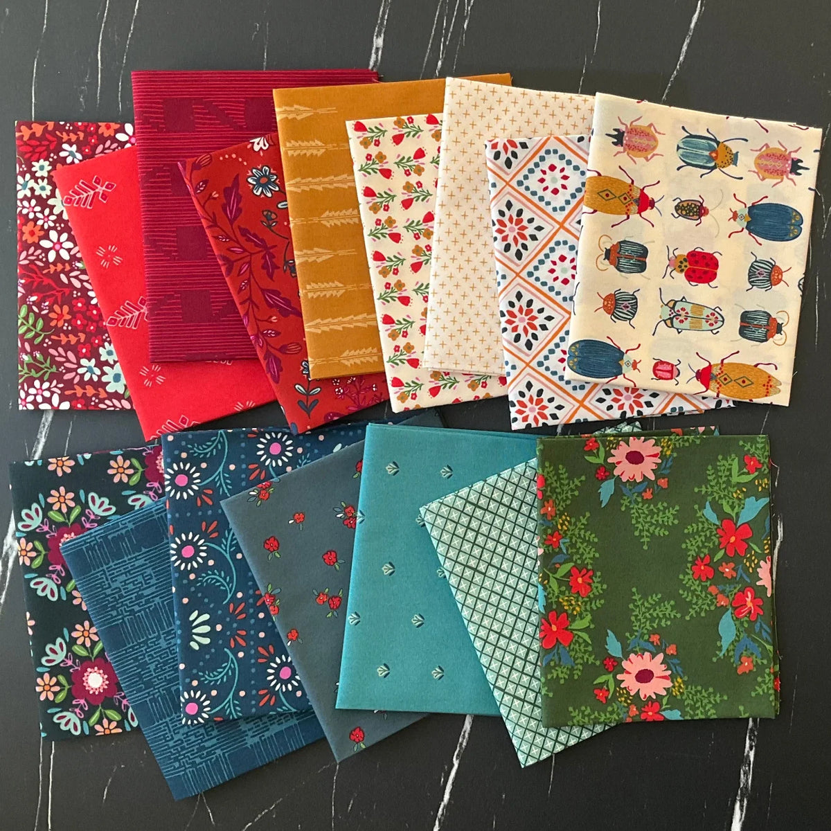 Assorted fabric squares stack in red, teal, green, and cream with floral and novelty prints