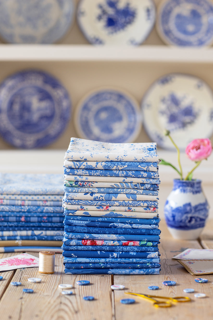 Stack of blue floral fabric fat eighths with cream wrap ribbon for sewing