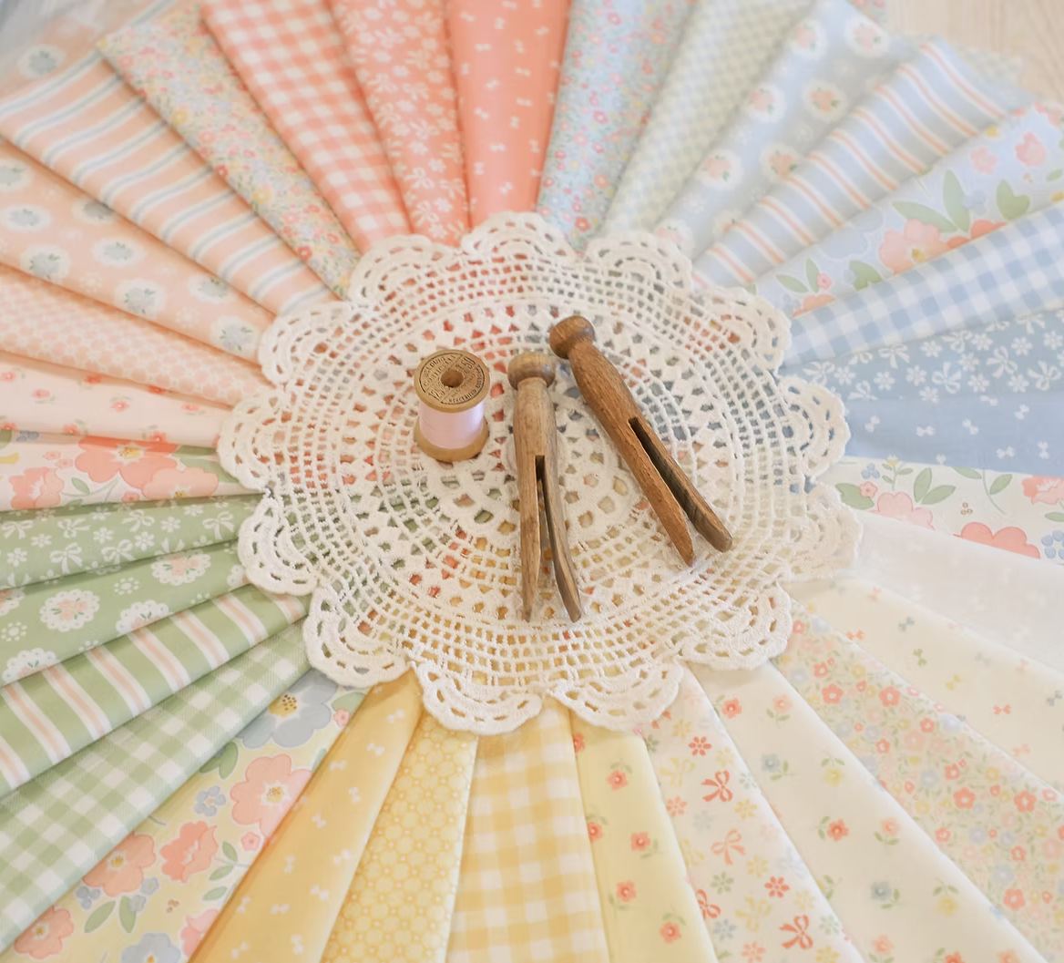 Pastel mini charm squares fanned with crochet doily and wooden sewing tools