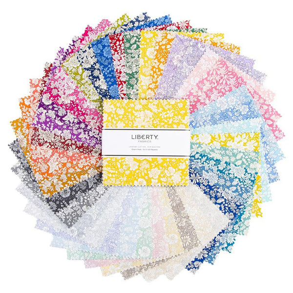 A charm square pack of Liberty Fabrics cotton piecing fabrics in a variety of dainty flowers,  with a yellow and white floral pattern in the centre, wrapped in a white paper band labeled 'LIBERTY FABRICS'.