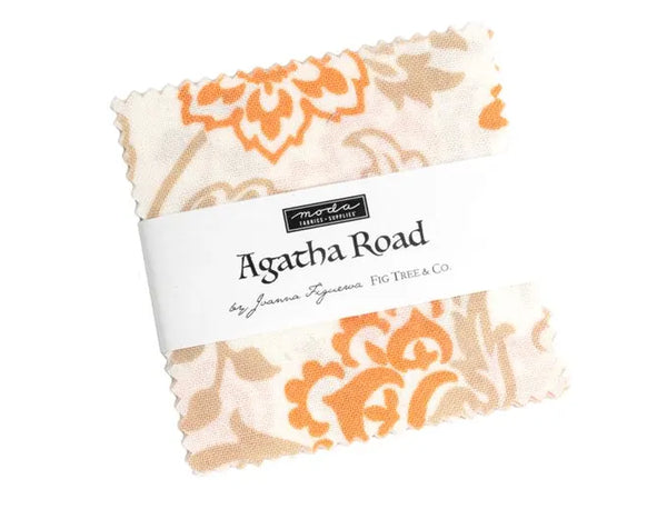 A charm square pack of fabric cut pieces with scalloped edges, featuring an orange and beige floral damask pattern on a white background, wrapped with a white paper label that reads 'marta fabric company' and 'Agatha Road by Joanna Syngmanas FIG TREE & CO.'.