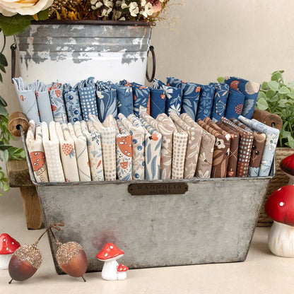 Stack of 2.5-inch nature-print fabric charm squares in blue and cream tones in a metal tray